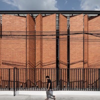 a man walks past a red brick building with a fence